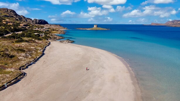 Una playa con aguas turquesas transparentes, una orilla arenosa y una pequeña isla con una torre.