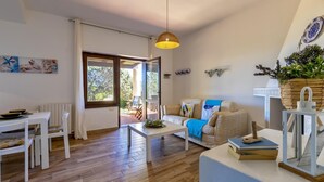 Una sala de estar con piso de madera, un sofá blanco, una mesa de comedor con sillas y una lámpara colgante.