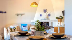 Un comedor con una mesa blanca, servida con cuencos y platos negros, una cesta de mimbre y una planta en maceta.