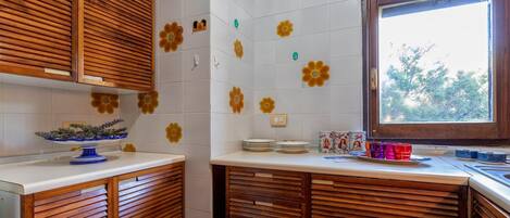 Una cucina con mobili in legno, piastrelle bianche decorate con motivi floreali e una finestra vista alberi.