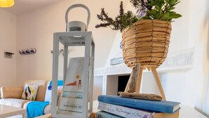 Una habitación con un sofá blanco, una mesa con un farol y una cesta, y una pila de libros.