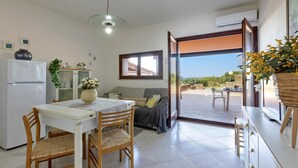 A compact living space with a dining area, kitchenette, and a sliding glass door leading to an outdoor patio. - Ss-m290-cdva0at - Villino Punta Negra (Stintino)