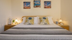 A neatly made bed with striped bedding, two decorative pillows, and a nightstand with a lamp and a small plant. - Ss-m290-cdva0at - Villino Punta Negra (Stintino)