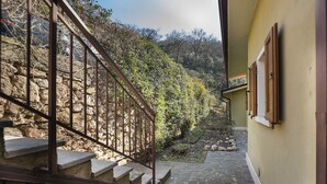 Eine steinerne Treppe führt einen Hügel hinauf, umgeben von Vegetation und einer Steinmauer.