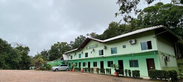 Un edificio de dos plantas con fachada verde y varias ventanas, con un automóvil estacionado adelante.
