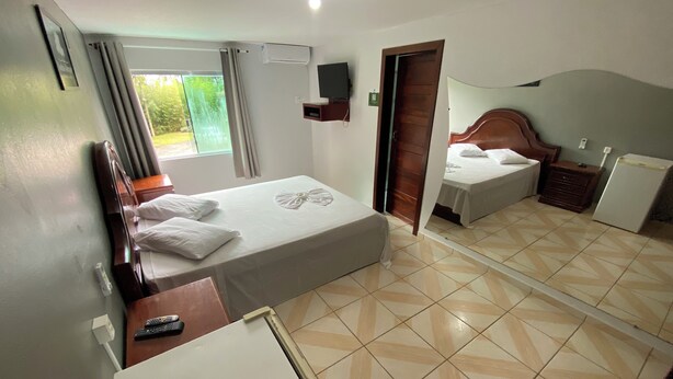 Une chambre d’hôtel avec un lit, un bureau, un miroir, une télévision et une fenêtre avec des rideaux.