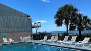 Une piscine à l’eau d’un bleu cristallin, entourée de chaises longues blanches et de palmiers.