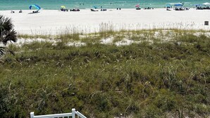 Une plage de sable blanc, avec une eau d’un bleu limpide et une vue sur l’océan. On y trouve des parasols et des chaises de plage.