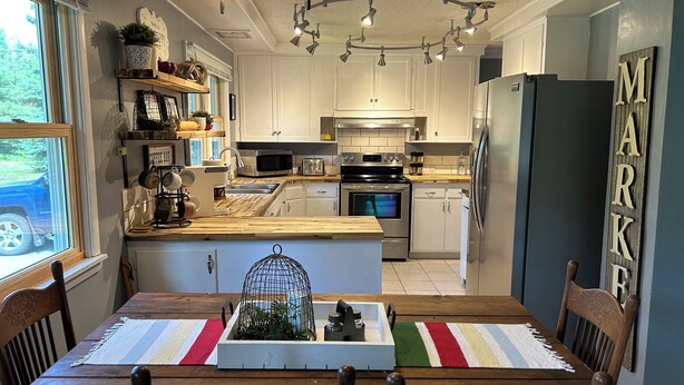 Een moderne keuken met witte kasten, een houten keukeneiland, roestvrijstalen apparatuur en een eethoek met een houten tafel en stoelen.