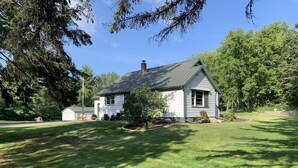 Een gelijkvloers huis met een groen dak en witte gevel, omgeven door een verzorgd gazon en bomen.