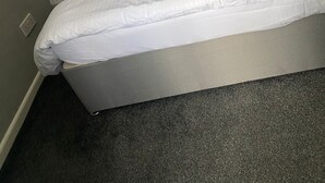 A neatly made bed with a grey blanket, two pillows with a geometric pattern, and a grey headboard. - Cosy, Modern Apartment (Darlaston)