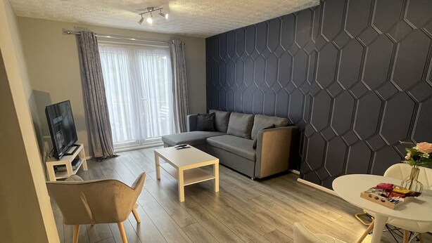 A modern living room with a sofa, coffee table, and chairs. There is a dining table with a vase and a remote control on a stand. - Cosy, Modern Apartment (Darlaston)