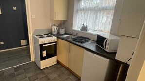 A compact kitchen with a gas stove, a built-in oven, a sink, and a window with sheer curtains. - Cosy, Modern Apartment (Darlaston)