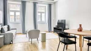 En moderne stue med en grå sofa, et rundt spisebord og et fjernsyn på et sort stativ.