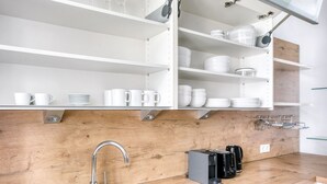 Et moderne køkken med hvide hylder, en træbordplade, en vask og en kaffemaskine.
