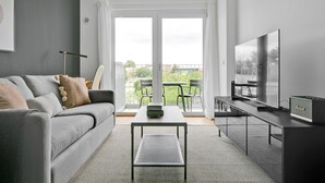 Moderni olohuone, jossa on harmaa sohva, sohvapöytä, televisio ja parveke, jossa on tuoleja.