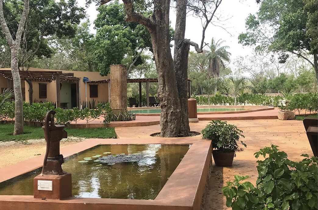 Un patio con una fuente, una estatua y un edificio con una pérgola.