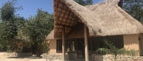 A thatched-roof building with a stone foundation, a small porch, and a stone wall with a circular design.