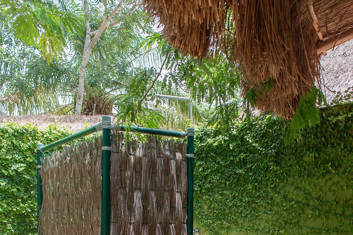 Une structure métallique verte, ornée d’un panier tressé suspendu, entourée de verdure et d’un mur de pierre.
