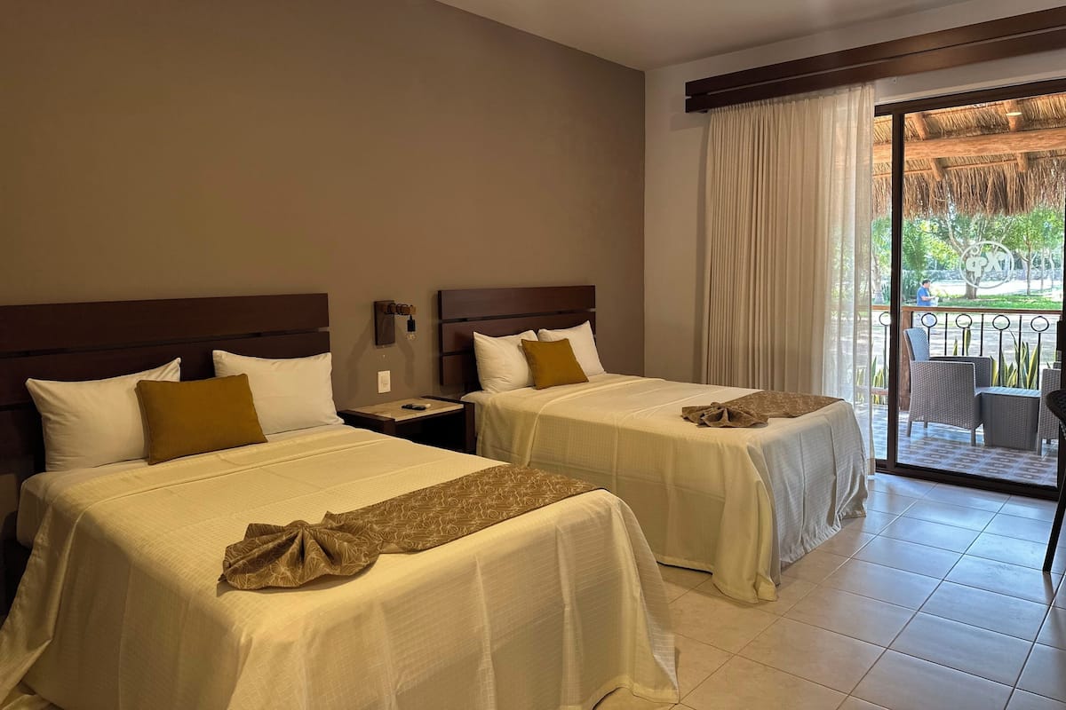 Une chambre d’hôtel avec deux lits, une table de chevet, une fenêtre avec des rideaux et une vue sur l’extérieur.