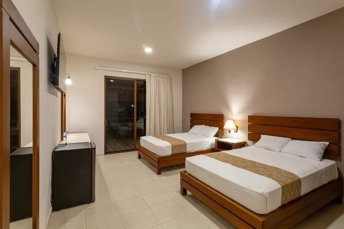 Une chambre d’hôtel avec deux lits, un bureau, une télévision et une porte-fenêtre coulissante donnant sur l’extérieur.