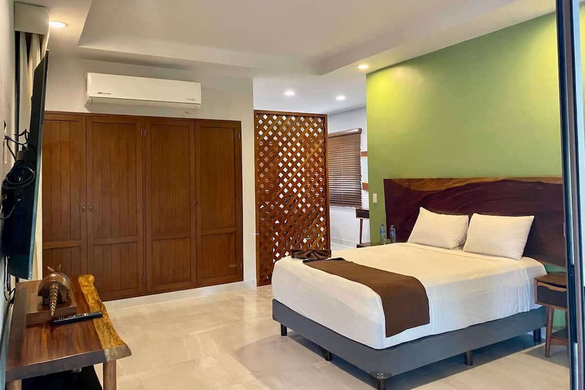 Une chambre d’hôtel moderne avec un grand lit, une armoire en bois et un élément de séparation décoratif.
