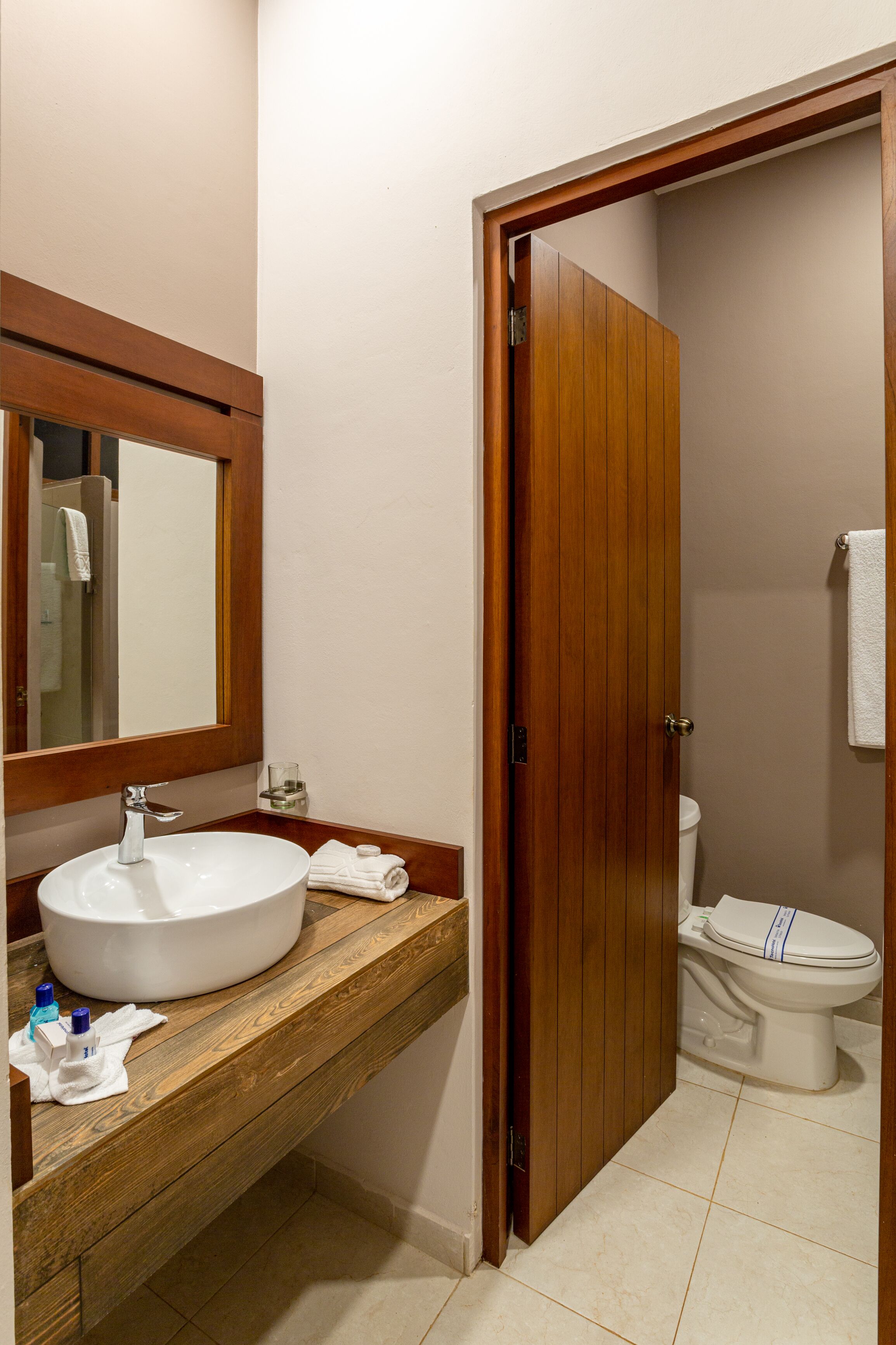 A bathroom with a wooden vanity, a sink, a mirror, and a toilet.