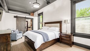 A bedroom with a large bed, wooden nightstands, a dresser, and a window with a view of greenery.