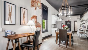 A modern kitchen with stainless steel appliances, a dining area with a wooden table and chairs, and a chandelier with exposed bulbs.