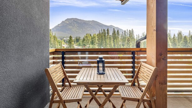 Eine Holzterrasse mit zwei Holzstühlen und einem Tisch, mit Blick auf einen Wald und Berge.