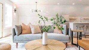 Een moderne woonkamer met een grijze bank, een ronde houten salontafel en een potplant.