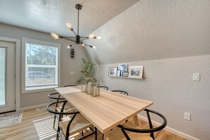 A dining area with a wooden table, black chairs, a ceiling light fixture, and framed pictures on the wall.