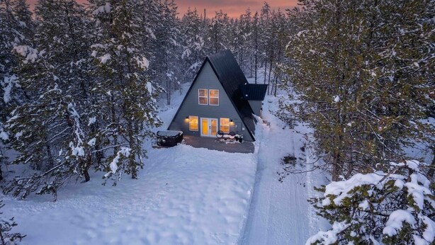 Een chalet met een schuin dak, omringd door met sneeuw bedekte bomen, en een helder pad naar de ingang.