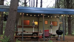 Ein Wohnmobil mit überdachtem Picknicktisch und Grill, umgeben von Bäumen.