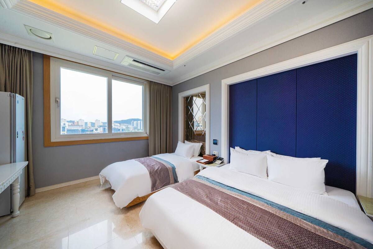 Ett hotellrum med två sängar, ett skrivbord, ett fönster med utsikt över staden och en stor blå sänggavel.