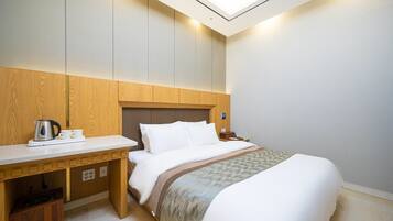 A hotel room with a bed, a wooden desk, a nightstand, and a skylight.