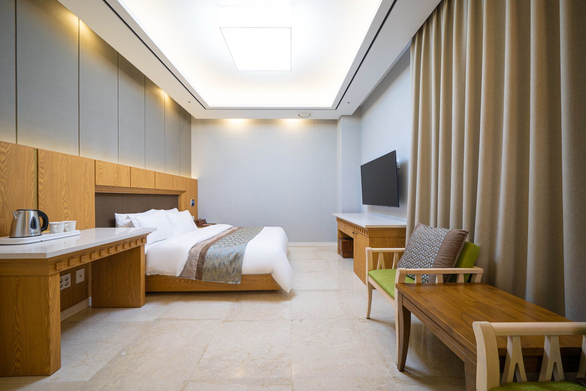 Habitación de hotel con cama, escritorio, silla, televisor y ventana grande con cortinas.