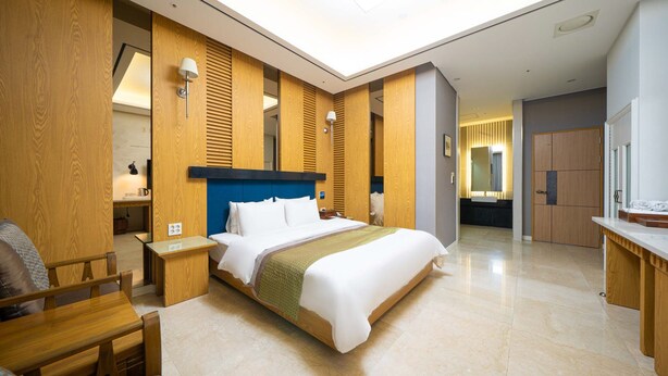 A modern hotel room with a large bed, wooden paneling, a skylight, a desk, and a bathroom visible in the background. - HOTEL CORE (Naju)