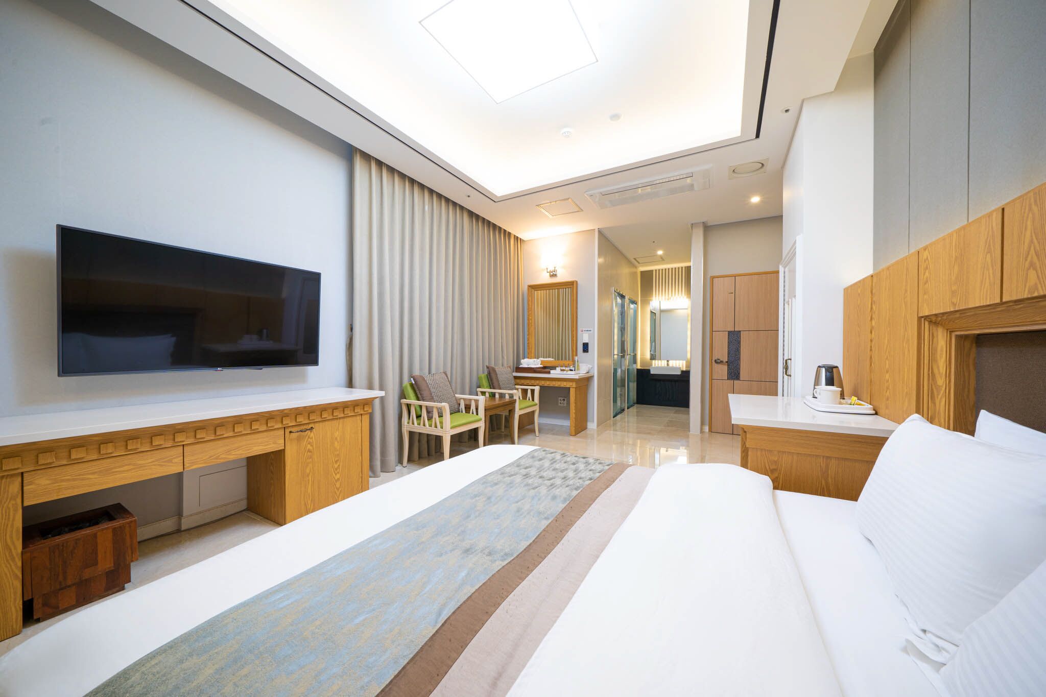 Habitació d'hotel moderna amb un llit gran, una televisió penjada a la paret, un escriptori amb una cadira i una cuineta petita.