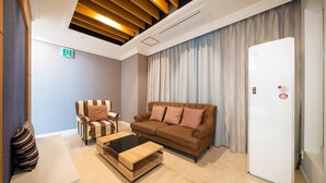 A modern hotel room with a brown sofa, a striped armchair, a wooden coffee table, and a white door. - HOTEL CORE (Naju)