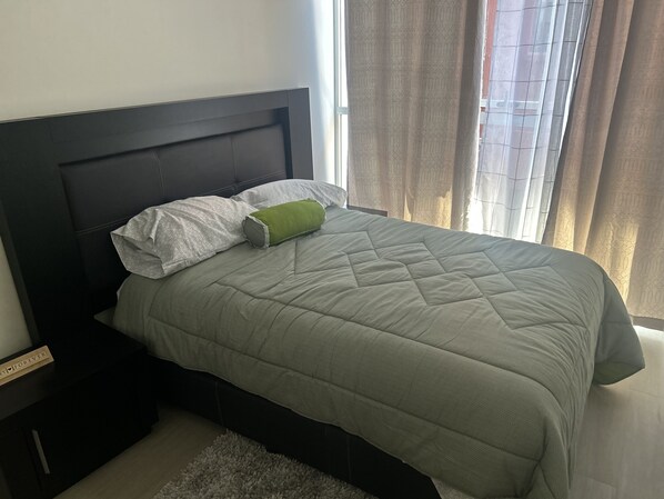 A neatly made bed with a green quilt, a white pillow, and a green accent pillow.