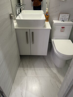 A bathroom with a white sink, toilet, and cabinet. There is a sign on the toilet and a bottle of hand sanitizer on the sink.