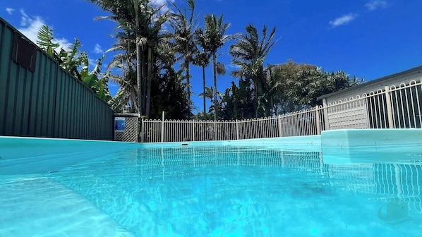 A clear swimming pool with a metal fence, surrounded by palm trees and a clear blue sky. - Caves Getaway - pool, beach, DOG friendly & air-conditioned for comfort (Caves Beach)