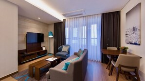 A modern living room with a sofa, coffee table, TV, and dining area. - Merciel Hotel (Busan)