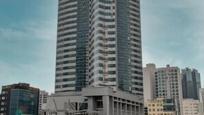 A tall, modern skyscraper with a curved design, surrounded by other buildings. - Merciel Hotel (Busan)