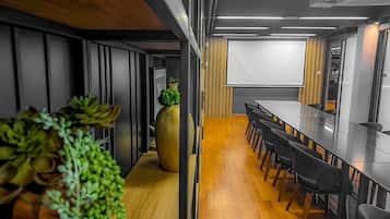 Una sala de conferencias moderna con una mesa larga, sillas negras, una planta en maceta grande y una pizarra.