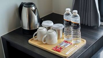Una bandeja de madera con una tetera, dos termos, dos botellas de agua, un paquete de galletas y una cuchara sobre una encimera oscura.