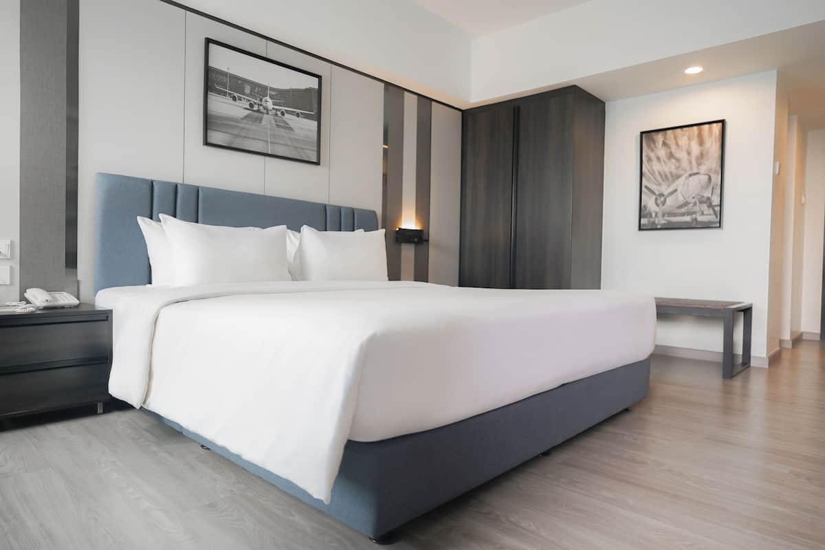 Une chambre d’hôtel moderne avec un grand lit, une table de chevet, un téléphone fixé au mur et un tableau encadré accroché au mur.