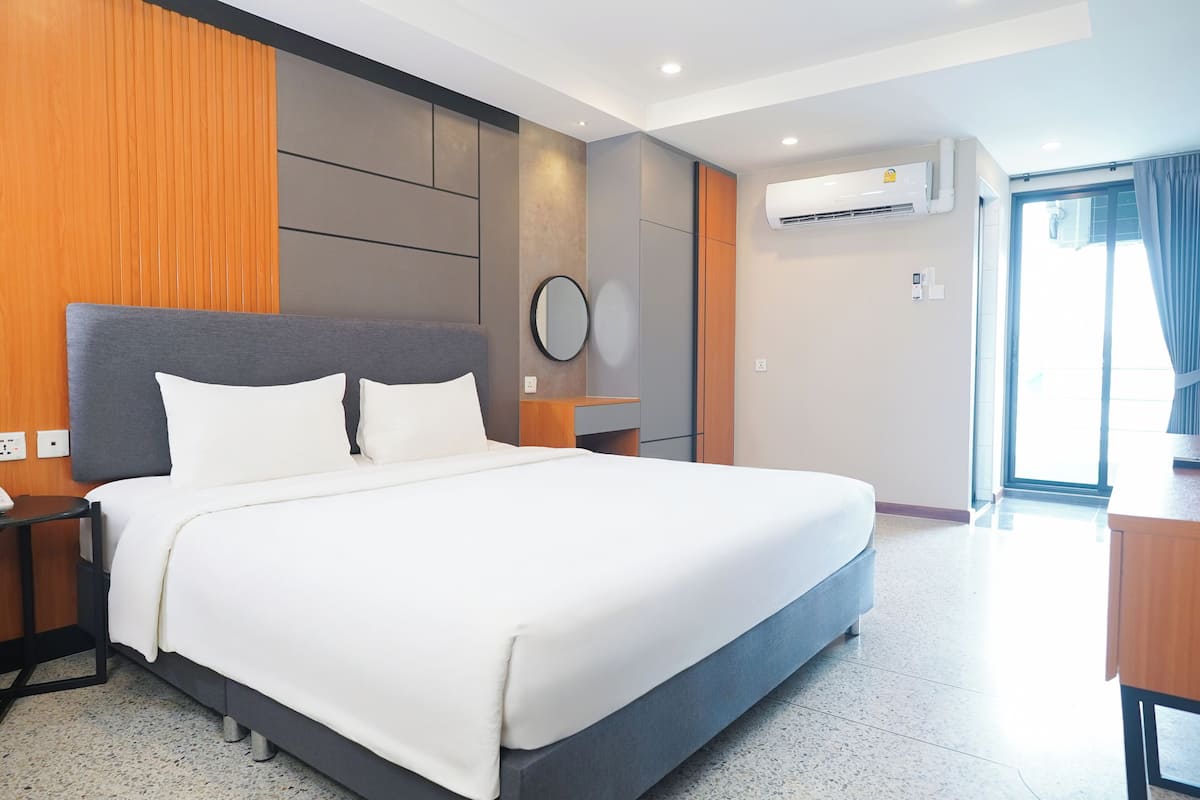 Une chambre d’hôtel moderne dotée d’un grand lit, d’une table de chevet, d’un miroir, d’un appareil de climatisation et offrant une vue sur l’extérieur.