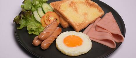 A plate with toast, ham, a fried egg, sausages, lettuce, and cucumber slices.